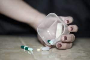 Hand resting on the floor holding a container, pills spilling out