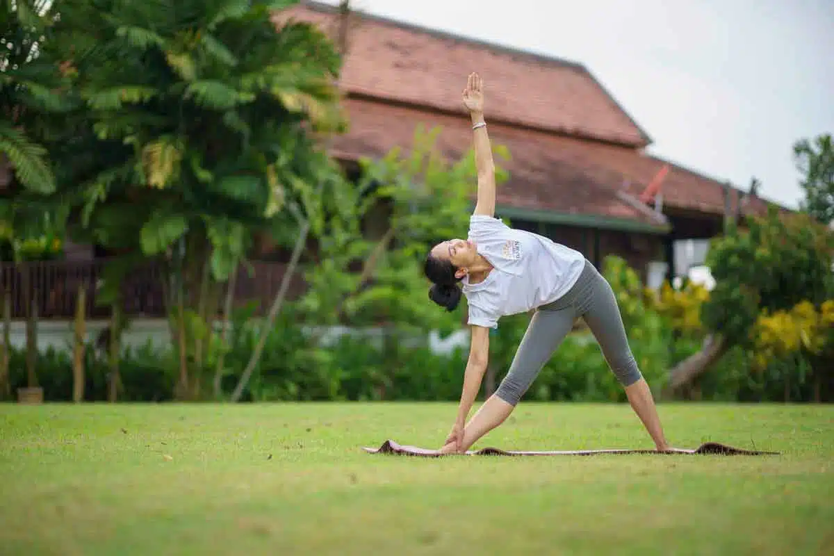 A woman practicing the Triangle Pose on a yoga mat in a garden at The Dawn.
