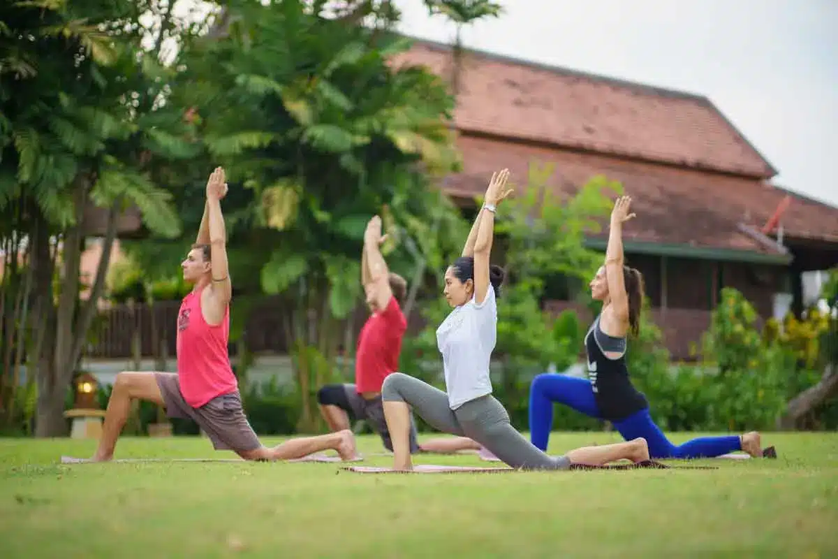 A group of four people practicing yoga in a lunge pose on a lawn at The Dawn.