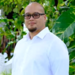 Portrait of Paolo wearing glasses and a white shirt among green leaves