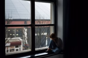 child-sitting-sadly-on-a-window-sill-looking-out-at-a-gloomy-cityscape