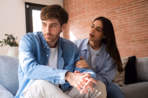 a-young-man-and-a-young-woman-sitting-on-a-sofa-in-a-living-room-engaged-in-a-serious-or-tense-conversation.avif