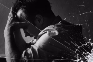 Black and white view of a distressed man holding his head behind cracked glass