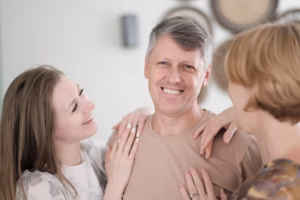 Smiling middle-aged man with two family members resting their hands on his shoulders