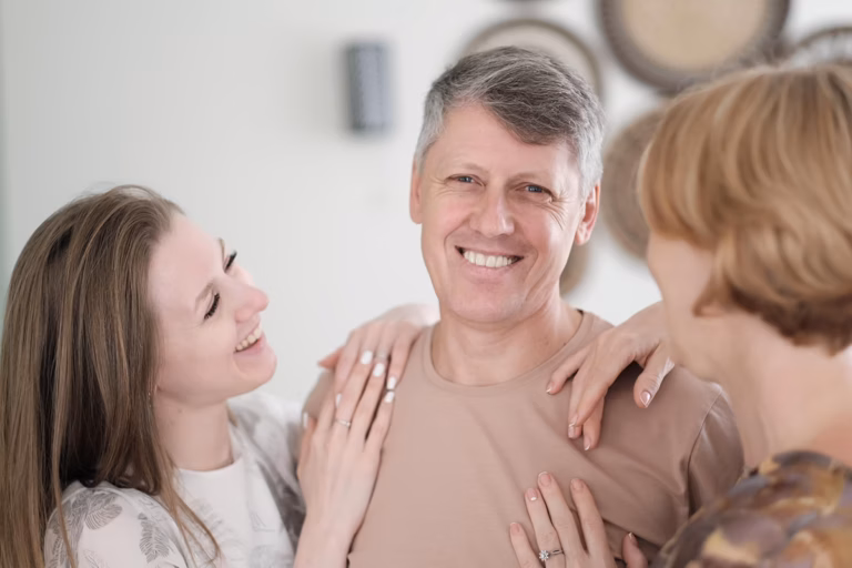 Smiling middle-aged man with two family members resting their hands on his shoulders
